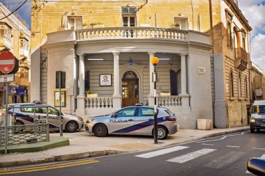 Sliema, Malta - 11.03.2025: Geleneksel bir Malta polis karakolu binasının önüne park etmiş polis arabaları taş mimarisi ve şehir caddesi ile gündüz vakti.