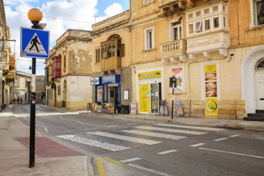 Sliema, Malta - 11.03.2025: A sunny Maltese street featuring traditional yellow buildings with wooden balconies, shop windows, a 