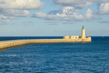 Ricasoli Dalgakıranı ve tarihi deniz feneri kulesinin Valletta 'nın Grand Harbour, Malta girişindeki parlak, bulutlu gökyüzünün altındaki manzarası..