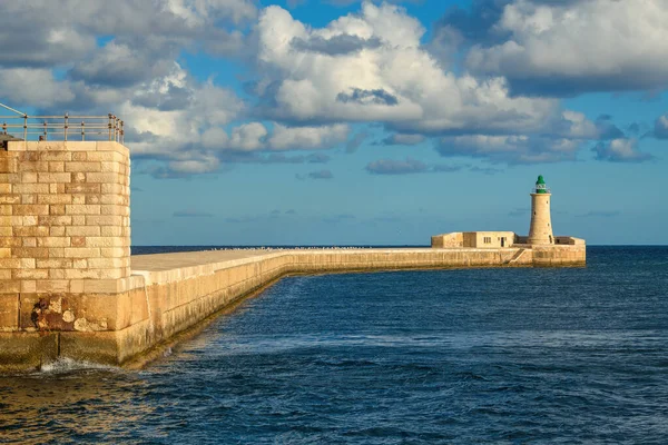Ricasoli Dalgakıranı ve tarihi deniz feneri kulesinin Valletta 'nın Grand Harbour, Malta girişindeki parlak, bulutlu gökyüzünün altındaki manzarası..