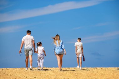 Beyaz ve mavi elbiseli dört kişilik bir aile sıcak ve kuru bir kayalık çölde mavi gökyüzüne doğru yürür..