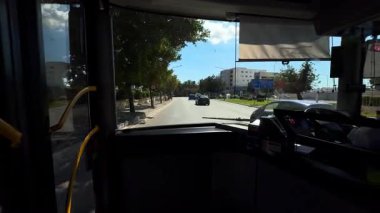Zabbar, Malta - 1 Haziran 2025: POV, şehirden geçen bir otobüs durağından çeşitli yolcuların araca bindiği bir otobüs durağına doğru çekildi. Ağaçları ve tarihi mimarisi olan manzaralı şehir yolu.