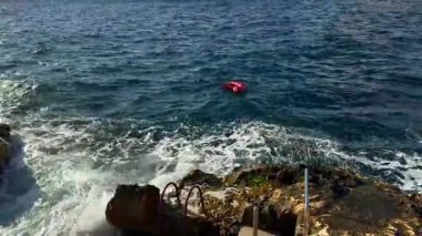 Mavi deniz dalgaları üzerinde kırmızı ve beyaz bir dalgıç ile zıpkınla balık avlayan bir şamandıra, kayalık kıyılarının yakınındaki bir dalgıcın teknelerini uyardı..