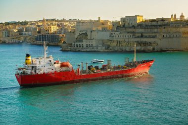 Valletta, Malta - 17 Ocak 2026: Büyük limanın turkuaz sularında ilerleyen büyük bir kırmızı tanker gemisi ve arka planda tarihi şehir tahkimatları bulunuyor..
