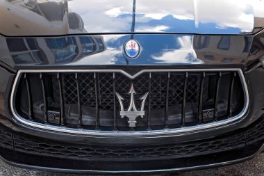 Sliema, Malta - 5 Kasım 2025: Gökyüzü yansımalı parlak bir kaput ve şehir caddesinde park edilmiş siyah lüks Maserati arabasının ikonik gümüş mızrak logosu.