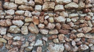 Düzensiz şekilli büyük doğal taşlardan yapılmış antik bir duvara yakın plan. Kaba yüzeyli, sıcak toprak tonlarında taş işçiliğinin detaylı dokusu.