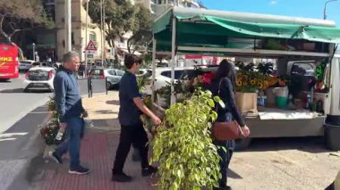 Sliema, Malta - 2 Şubat 2026: İnsanlar güneşli bir günde bir otoparkta renkli çiçek buketleriyle gezici bir çiçek standının önünden geçiyor.
