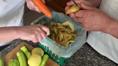 Havuç ve patatesleri yeşil bir organik atık kutusuna sokan kadın ve erkek ellerinin yakın çekimi. Ortak aile yemekleri ve çevre dostu mutfak alışkanlıkları..