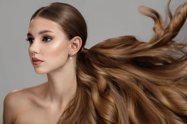 Uzun dalgalı ve parlak saçlı güzel, modaya uygun genç bir kadın. Esmer, kıvırcık saçlı.