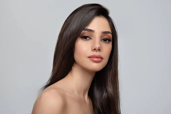 Gri arka planda düz siyah saçlı ve makyajlı bir kadının portresi.