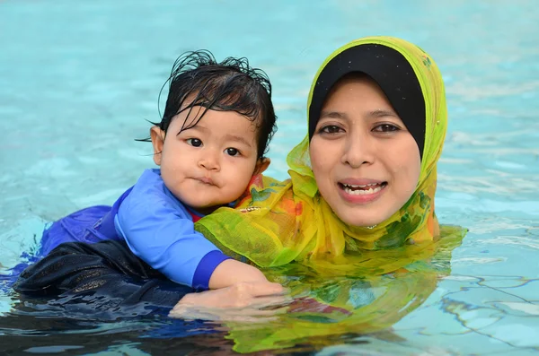 Vacker ung asiatiska muslimska mamma njuter undervisning henne söt baby flicka en första lektionen bad i en pool — Stockfoto