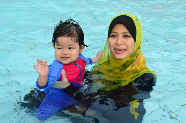 Vacker ung asiatiska muslimska mamma njuter undervisning henne söt baby flicka en första lektionen bad i en pool — Stockfoto