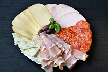 Peynir ve meze karışımı bir şey hazırla. Koyu ahşap arka planda salam, peynir, pastırma ve zeytin dilimleme tahtası. Yukarıdan bak. Siyah arka plan. Üst görünüm