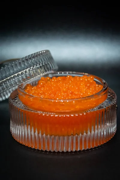 Close up de caviar vermelho salgado em um vidro em um fundo preto. — Fotografia de Stock