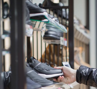 Ayakkabı alan genç bir adam. Ayakkabı mağazasından ayakkabı seçen bir müşteri. Ayakkabıcıda alışveriş yaparken erkek ayakkabısı seçiyor. Perakende mağazasındaki mutlu müşteri. Rafta ürün satışı.