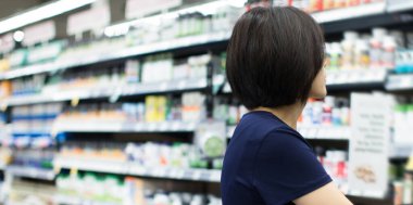 Market Eczanesinden Kadın Alışverişi. Süpermarkette alışveriş yapan biri. Kadın Tutucu Sepeti, hangi ürünü alacağına karar vermeye çalışıyor. Perakende Sağlık Sigortası, Vitamin ve İlaveleri.
