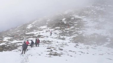 Yürüyüşçüler kış dağı yürüyüşü sırasında yoğun siste kayalık ve karlı bir yamaçtan dikkatlice inerler. Soğuk hava ve engebeli arazi macera ve aşırı koşullar yaratıyor..