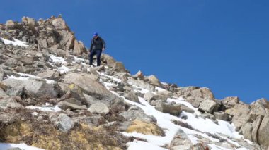 Bir yürüyüşçü, açık bir kış gününde kısmen karla kaplı dik kayalık araziye dikkatle iner. Sahne, açık hava macerası, fiziksel çaba ve dağ keşfi içeriyor..