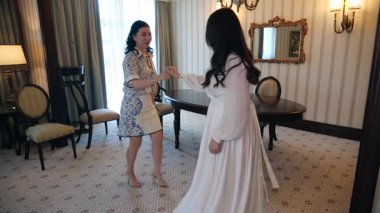 Göz kamaştırıcı elbiseli iki genç kadın dans ediyor, gülüyor ve lüks bir iç mekanda kaygısız bir anın tadını çıkarıyor. Hafiflik, dostluk ve hareket halindeki neşe. 4K ağır çekimde yakalandı.