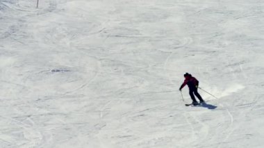 Siyah ve kırmızı bir kayak ceketi, kask ve gözlük takan bir adam kar kaplı bir yamaçta kayak yapıyor ve keskin bir dönüş yapıyor. Kayakları kar püskürterek dinamik bir çekim yaratıyor. 4K eş zamanlı