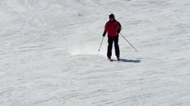 Kırmızı kışlık ceketli, kasklı ve gözlüklü bir adam kayak pistinde kayıyor. Dinamik 4K görüntüleri kayağın hız, kontrol ve keyif duygusunu yakalar..