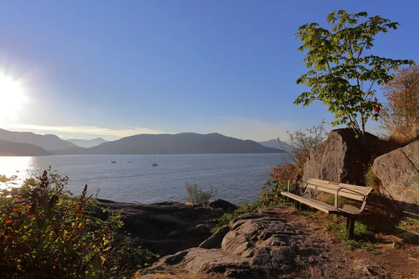 The bench on cliff in rays of the evening sun with view on the bay — Stock Photo, Image