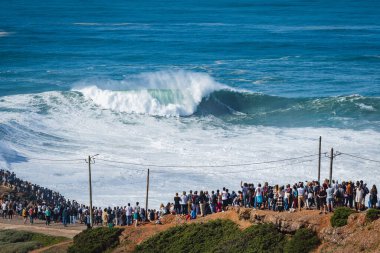 İnsanlar, Portekiz, Nazare 'deki Praia do Norte plajında dev dalgalarda sörf yapan büyük dalga sörfçülerini izliyor. Nazare, dünyanın en büyük dalgalarına sahip olmasıyla ünlüdür..