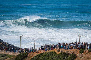 İnsanlar, Portekiz, Nazare 'deki Praia do Norte plajında dev dalgalarda sörf yapan büyük dalga sörfçülerini izliyor. Nazare, dünyanın en büyük dalgalarına sahip olmasıyla ünlüdür..