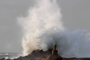Büyük deniz dalgaları jeodezik işaretler gören uçurumların üzerinden süzülüyor. Kuzey Portekiz kayalık kıyıları.