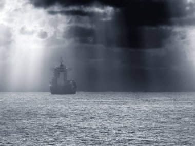 Güneş ışınlarıyla fırtınalı bir günbatımında okyanusu geçen ticari gemi; gelişmiş gökyüzü