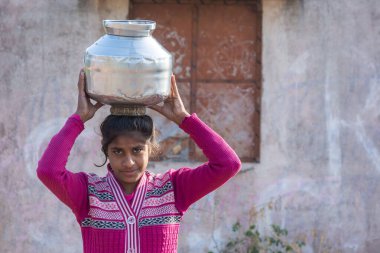 TIKAMGARH, MADHYA PRADESH, INDIA - 23 HAZİRAN 2021: Kimliği belirsiz bir Hintli köy kızı geleneksel çömleklerde su taşıyor,.