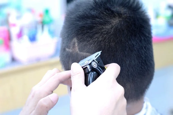 La coupe de cheveux du garçon avec tondeuse et rasoir dans le salon de coiffure — Photo