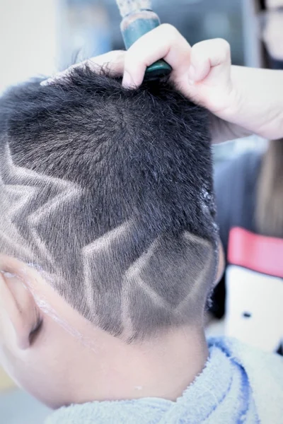 O corte de cabelo do menino com cortador e navalha na barbearia — Fotografia de Stock