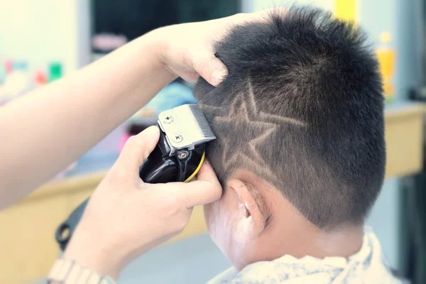 La coupe de cheveux du garçon avec tondeuse et rasoir dans le salon de coiffure — Photo