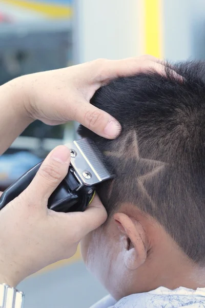 O corte de cabelo do menino com cortador e navalha na barbearia — Fotografia de Stock