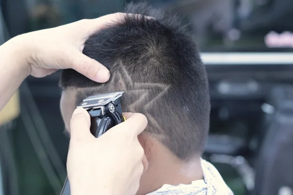 O corte de cabelo do menino com cortador e navalha na barbearia — Fotografia de Stock