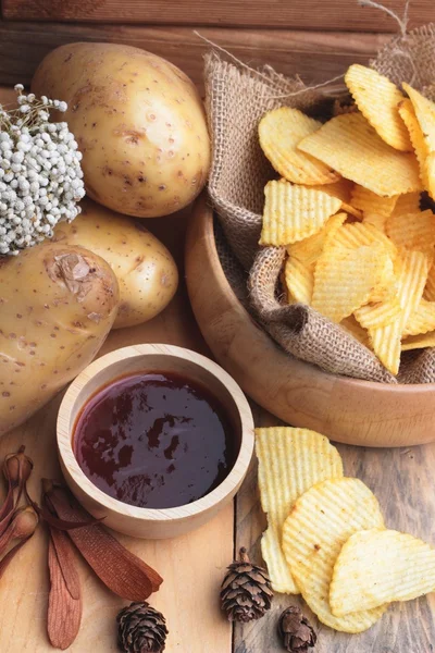 Potato chip and fresh potatoes on wood background