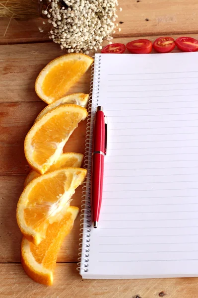 Libro diario con naranja y rodaja de tomate sobre fondo de madera . —  Fotos de Stock