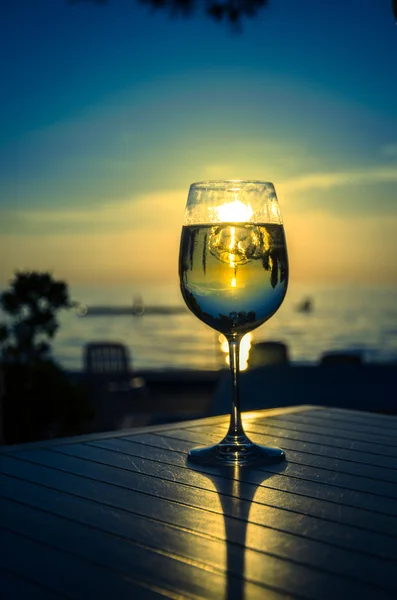 Copo de vinho e pôr do sol amarelo no litoral — Fotografia de Stock