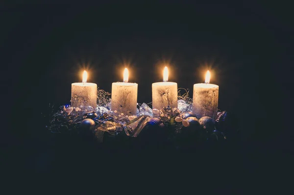 four burning advent candles with decoration and adornments on black background copy space