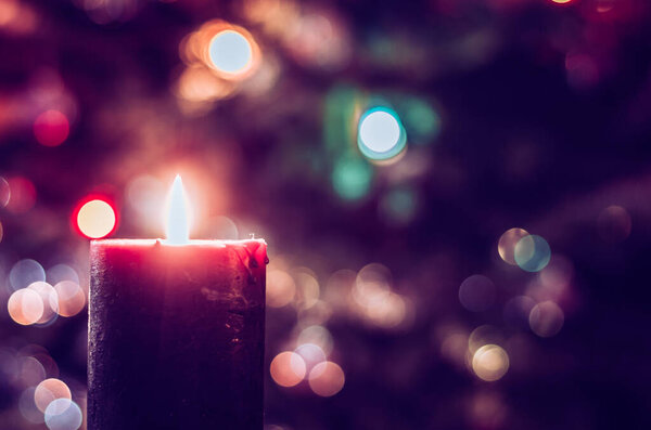 одна горящая свеча концепция с сияющими боке сверкающими лигами на елке на темном фоне