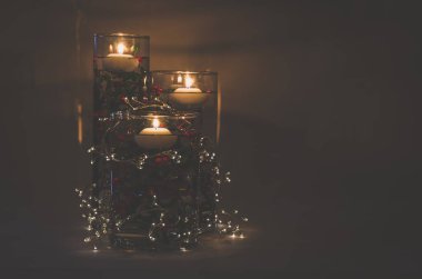 Su dolu vazoda süzülen mumlar ve renkli çiçekler.