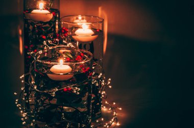 Su dolu vazoda suyun üzerinde mum yakmak ve arka planda parlak küçük ışıklarla renkli çiçekler.