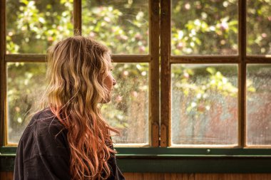 Güzel sarışın, gülümseyen kız pencerenin kenarında oturuyor ve bakıyor, sihirli pastel tonu efekti.