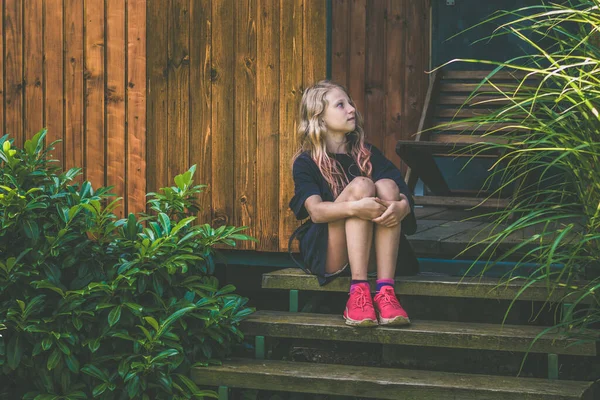 Adorable Blond Dziewczyna Siedzi Schodach Przy Drewnianym Domku Zielonym Ogrodzie — Zdjęcie stockowe