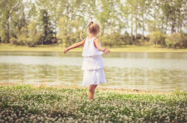 Sevimli sarışın kız yeşil çayırlarda eğleniyor ve güneşli yaz gününün tadını çıkarıyor.