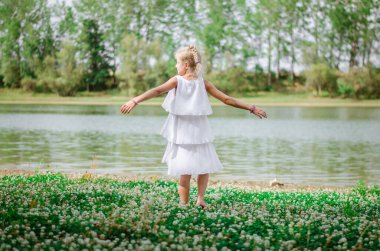 Sevimli sarışın kız yeşil çayırlarda eğleniyor ve güneşli yaz gününün tadını çıkarıyor.