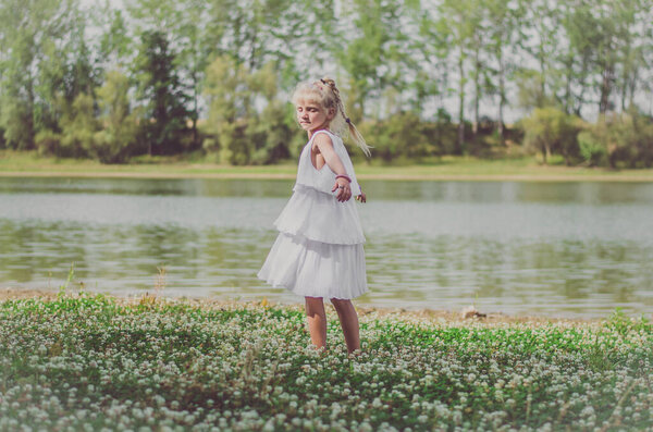 Adorable charming blond girl having fun in green floral meadow and enjoying summer sunny day
