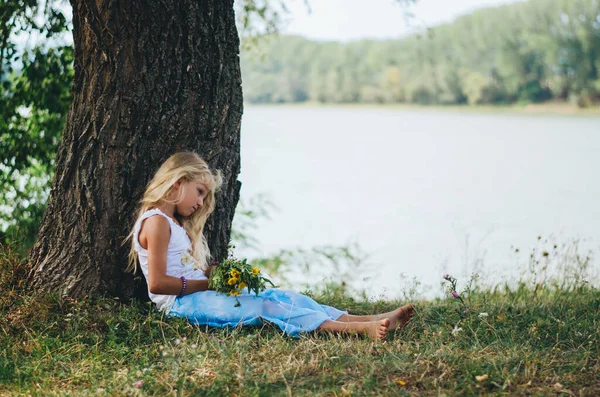 Uzun Sarı Saçlı Sevimli Çocuk Gölün Yanındaki Ağacın Yanında Oturuyor — Stok fotoğraf