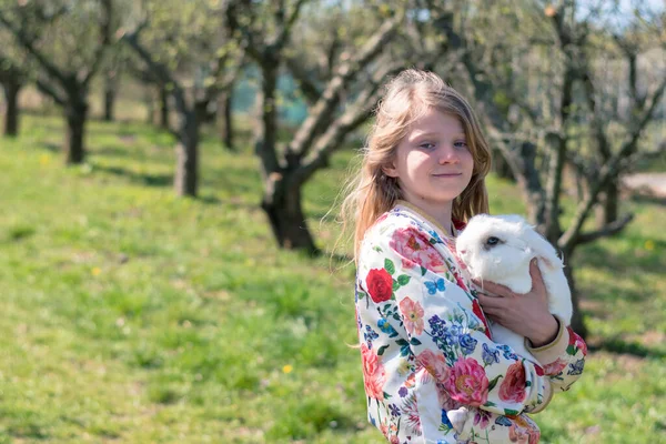 Küçük Kız Çimenlerde Oturuyor Beyaz Tüylü Bir Tavşana Sarılıyor — Stok fotoğraf